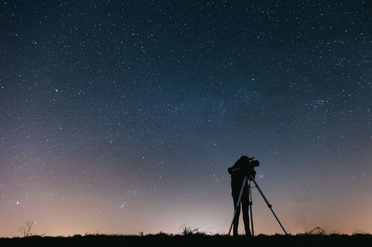 Silhouette of a person looking through a telescope against a night sky