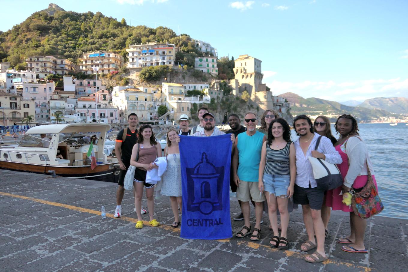 Central study abroad students on the Amalfi coast hold up a Central-logo banner.