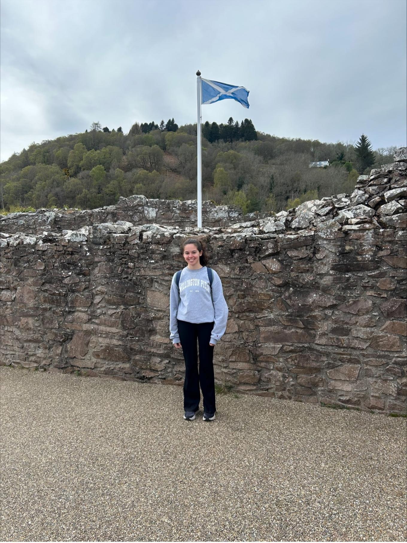 Grace Standing in front of stone wall, with Scottish flag behind