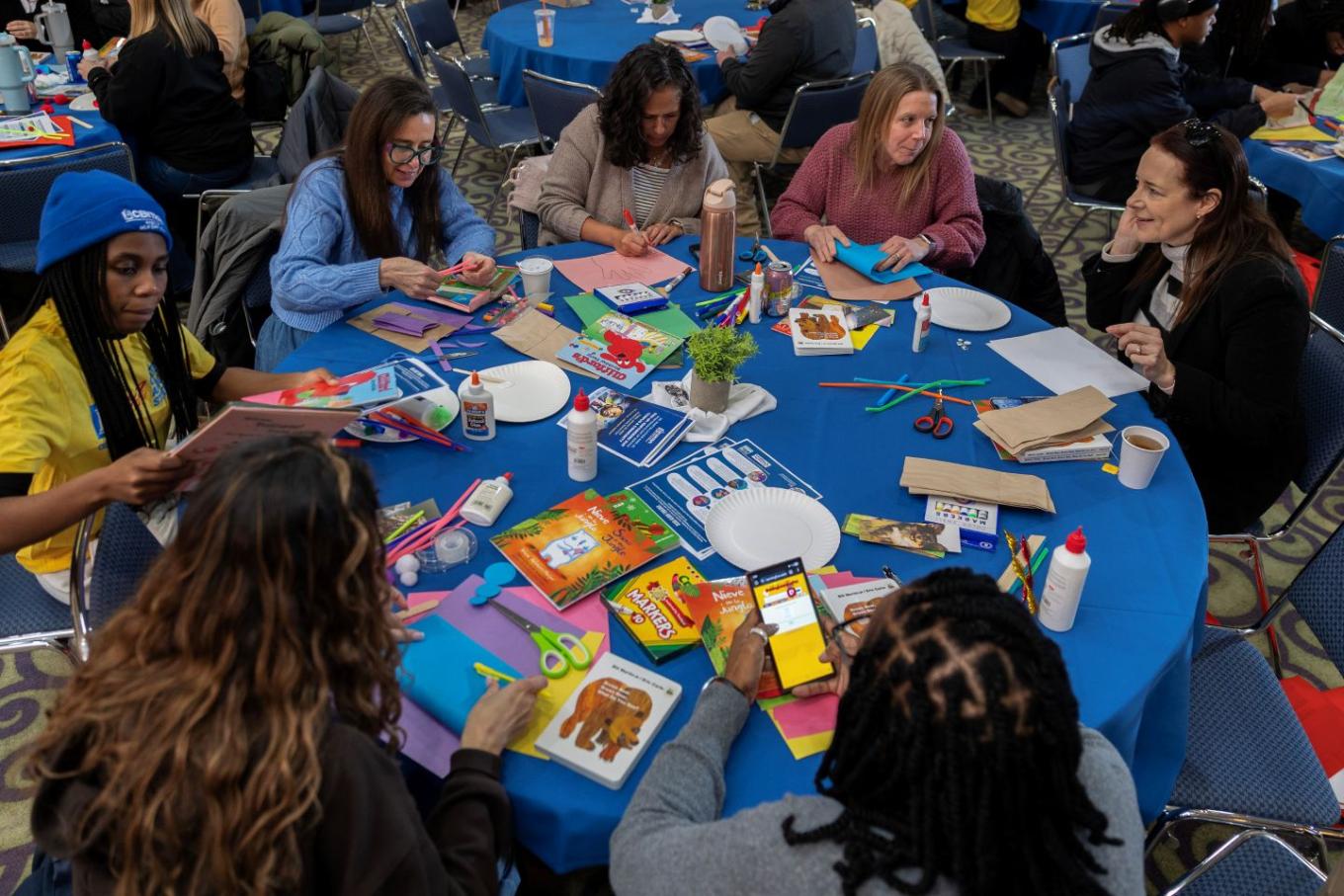 Students, faculty, and staff sit at a table assembling literacy kits.