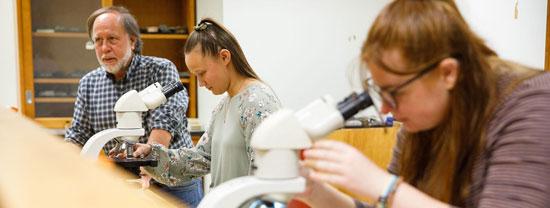 Students in class with teacher using microscope