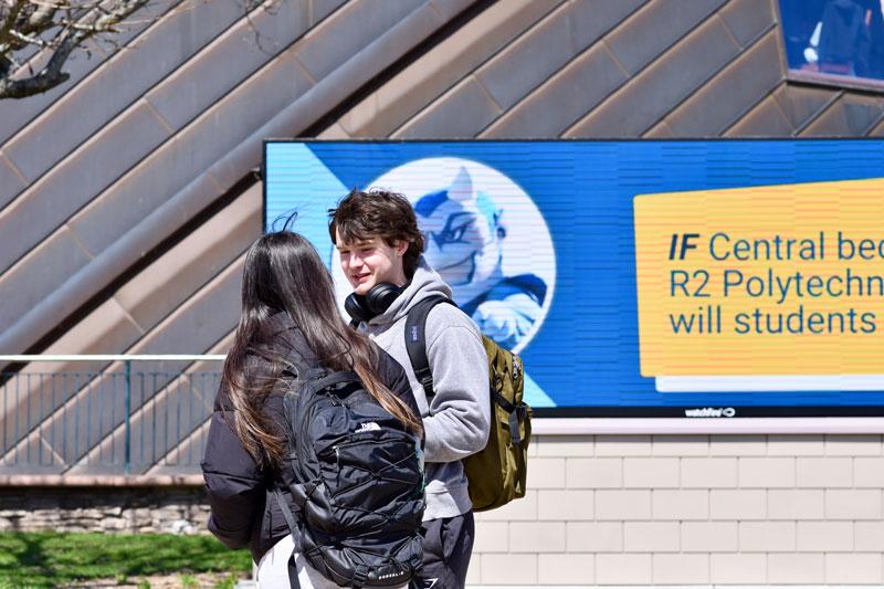 Students talking in front of video board with Kizer and R2 Polytech question