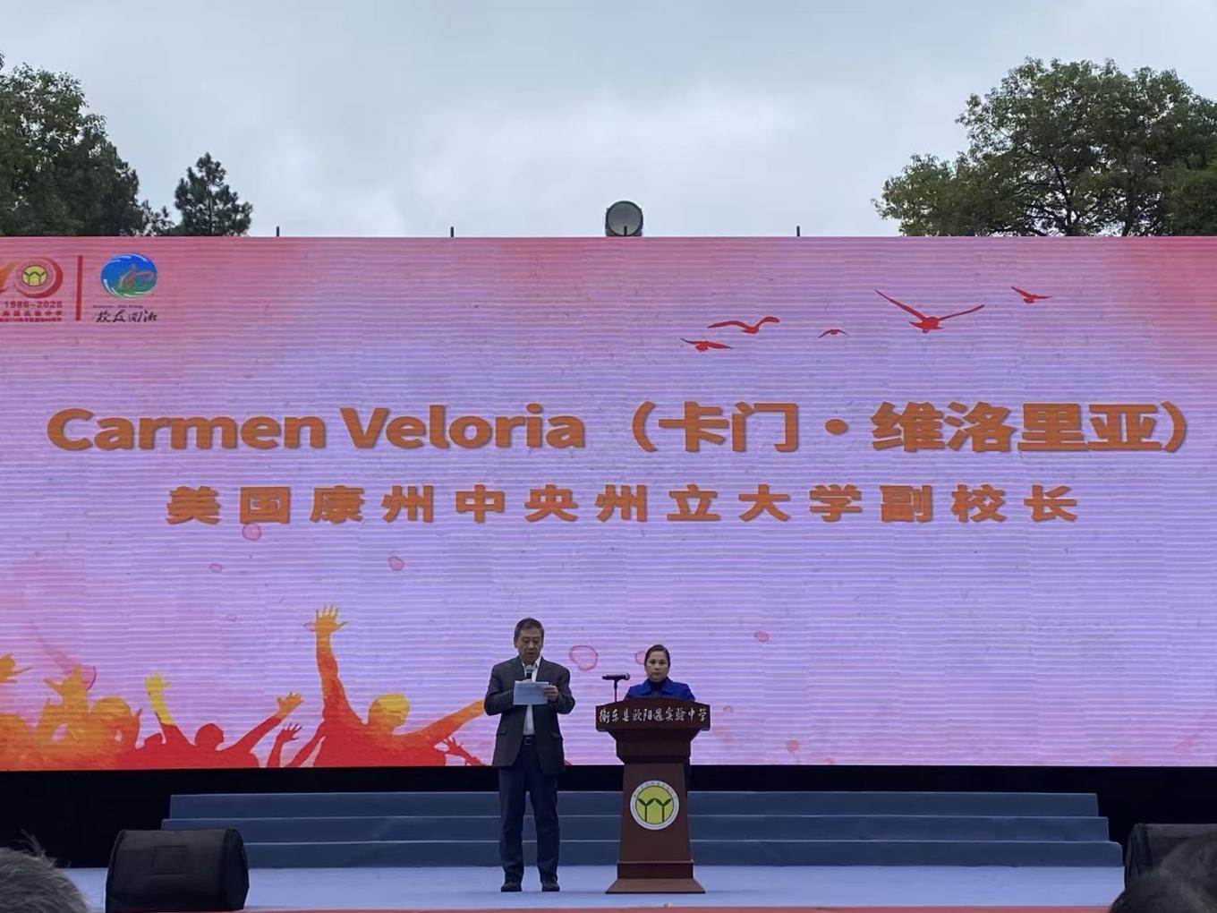 Dr. Carmen Veloria delivers remarks at the 40th anniversary celebration of the Ouyang Yu Experimental Middle School. Dr. Xudong Jia (left) translated her remarks into Chinese.