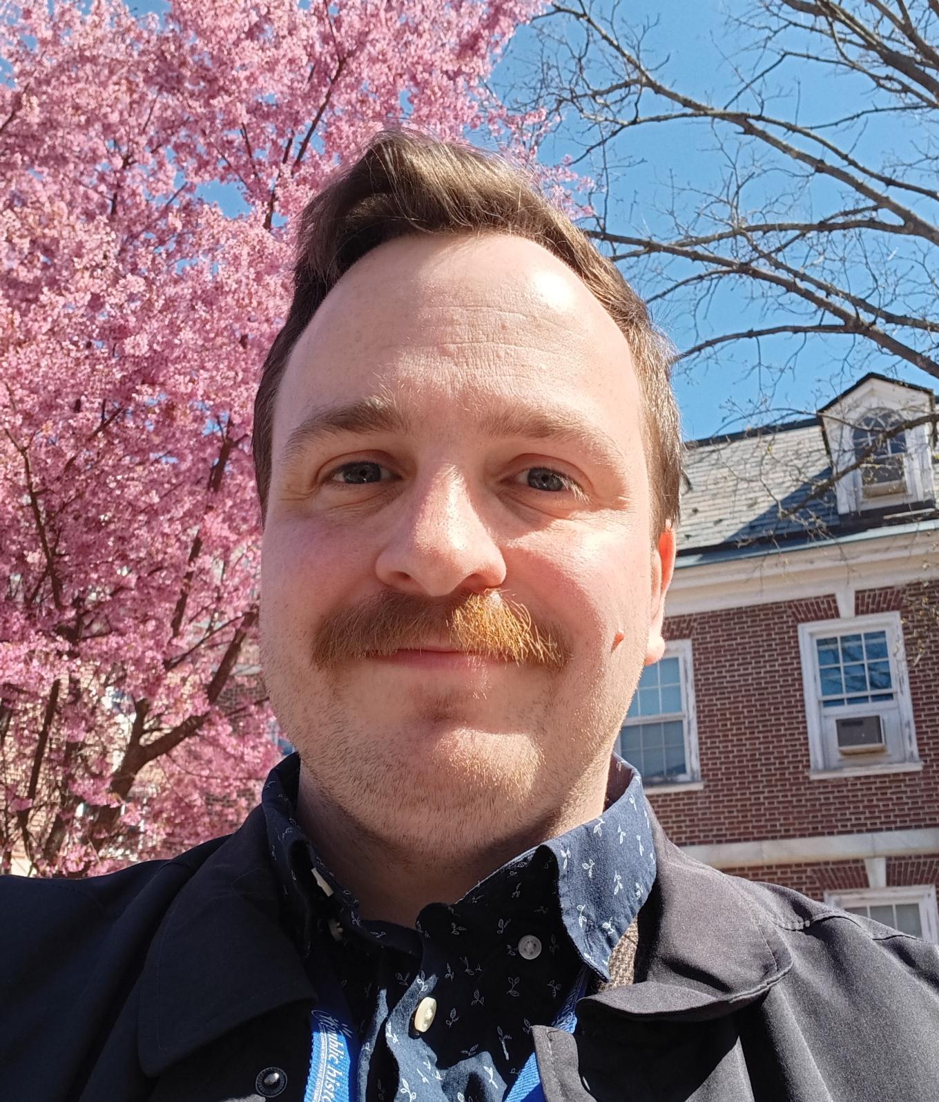 Professor Kynn smiling in front of blooming tree in spring