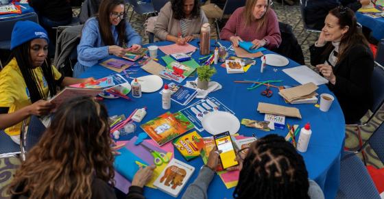 Students, faculty, and staff sit at a table assembling literacy kits.