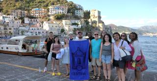 Central study abroad students on the Amalfi coast hold up a Central-logo banner.