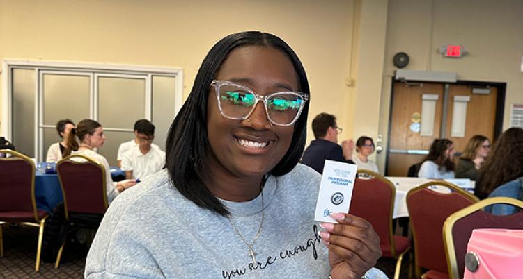 Woman smiling and presenting badge at the Professional Program for Education