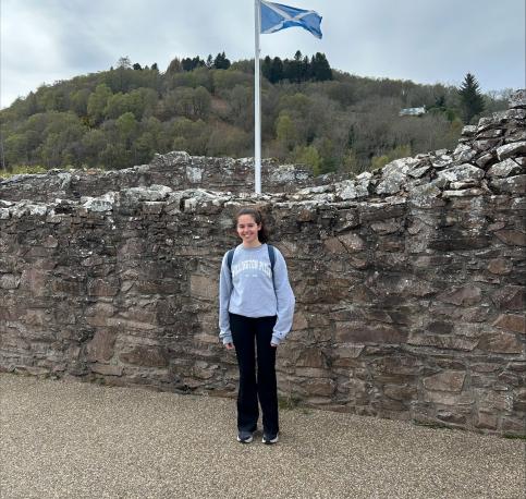 Girl standing in front of stone wall with Scottish flag above her
