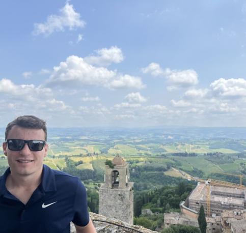 Student with sunglasses standing in front of vast Italian fields 