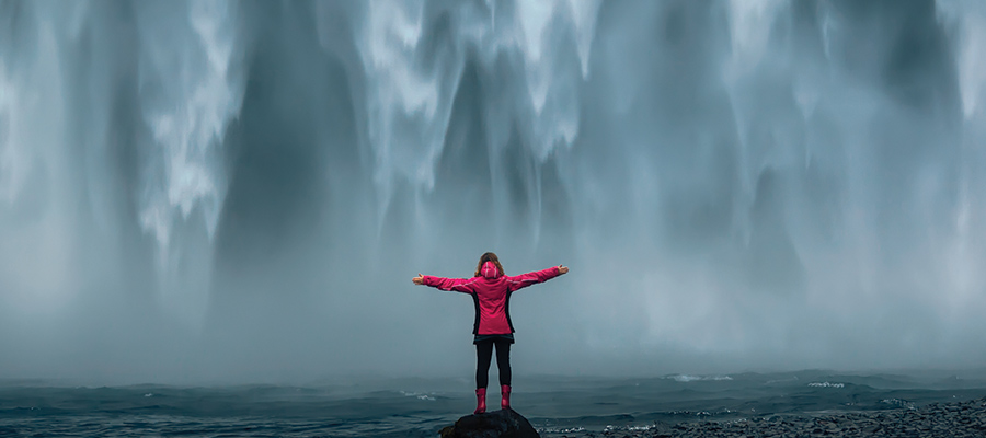 girl in a pink coat in front of icelandic waterfall